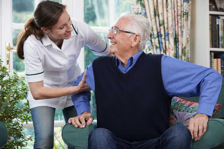 Older adult choosing breakfast while a caregiver reviews a daily routine at a bright dining table.